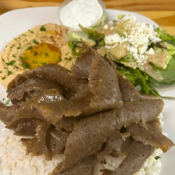 Mediterranean gyro plate with sliced meat, rice, hummus, a side salad, and white sauce.