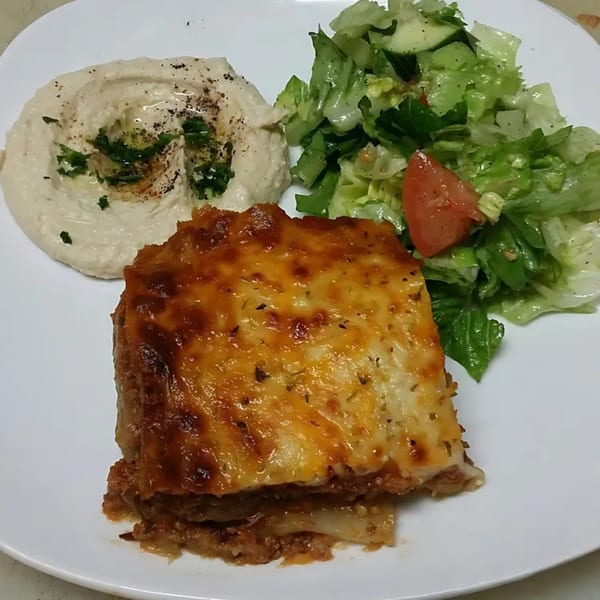 Moussaka with a side of hummus topped with parsley and a fresh green salad.