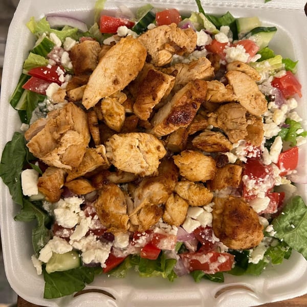 Close-up of a Mediterranean salad with grilled chicken, feta, tomatoes, cucumbers, and lettuce.