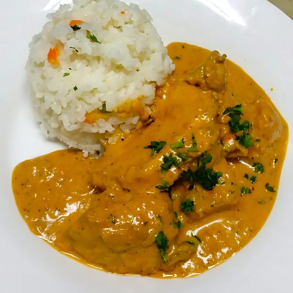 Creamy orange chicken curry with fresh parsley and a side of white rice on a white plate.