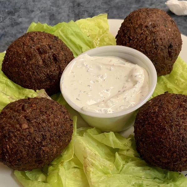 Four dark brown falafel balls on lettuce with a white dipping sauce in the center.