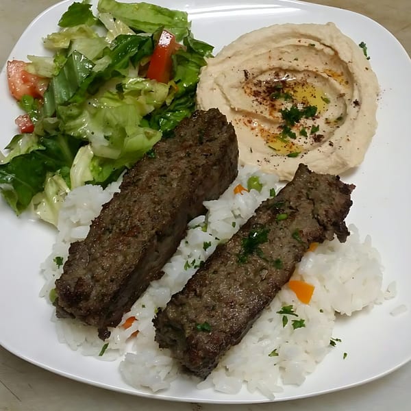 Two grilled Mediterranean beef skewers with rice, hummus, and a fresh green salad.