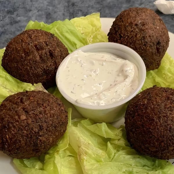 Four kibbeh on lettuce with a side of creamy white sauce, a Mediterranean dish from Blue Olive Grill.