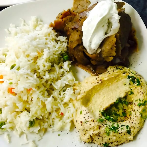 A Mediterranean plate with gyro meat topped with tzatziki, rice pilaf, and hummus with olive oil.